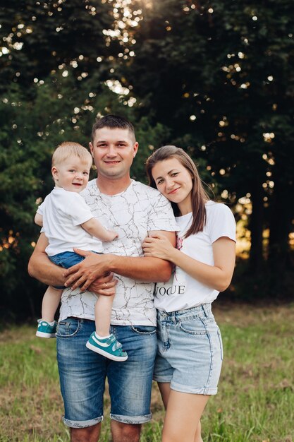 Picture of cheerful young caucasian female and male holds their child on hands, smiles and rejoices