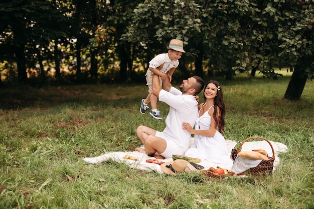 Picture of cheerful young caucasian female and male holds their child on hands, smiles and rejoices