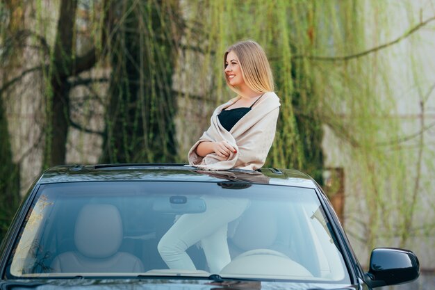サングラスをかけ、高級車のサンルーフに手を上げて陽気な若い女性の写真