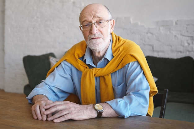 Free photo picture of confident successful attractive businessman in his sixties sitting at wooden desk in modern office interior, having serious facial expression. people, lifestyle, aging, business and fashion