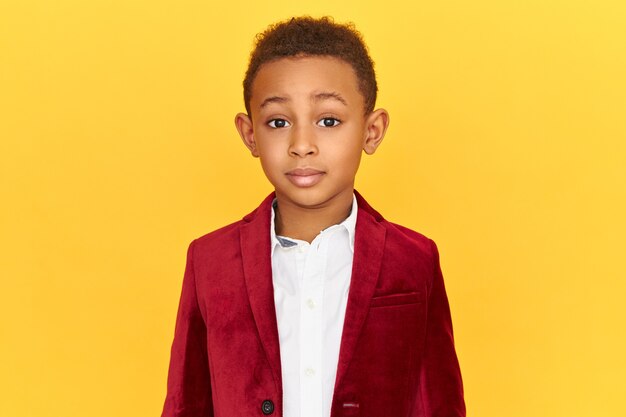 Picture of cute charming little Afro American boy wearing stylish clothes posing isolated looking at camera in fascination, astonished with big sale prices
