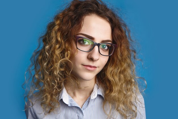 Picture of cute student girl wearing shirt and stylish glasses posing  before going to university. Attractive young female office worker in spectacles and formal wear smiling 