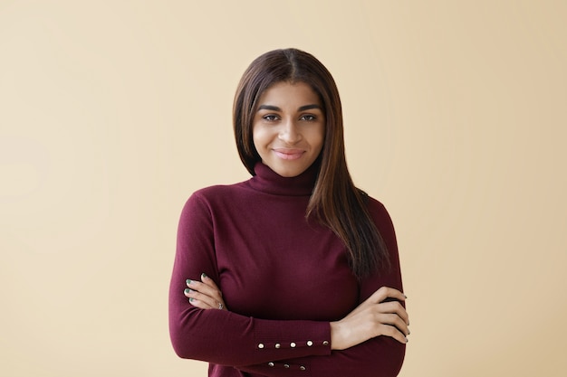 Picture of dissatisfied grumpy young Afro American woman with long straight hair expressing her disagreement, keeping arms folded, looking with serious skeptical facial expression