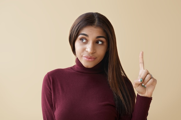 Picture of emotional young African American female looking away and pointing index finger up, having bright idea.