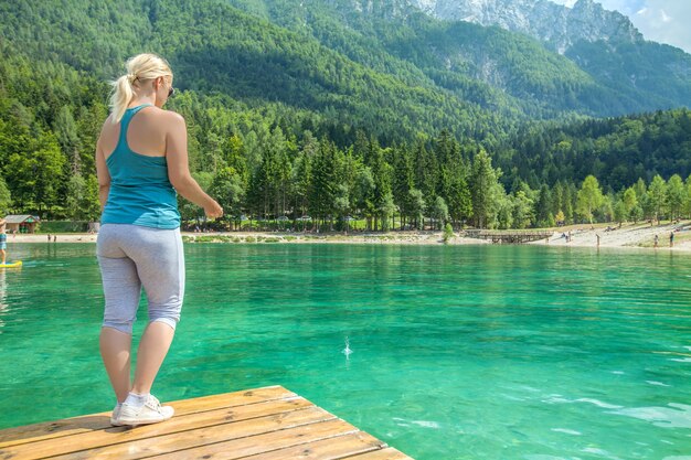 Picture of a female on a wooden bridge against an emerald lake with a breathtaking nature