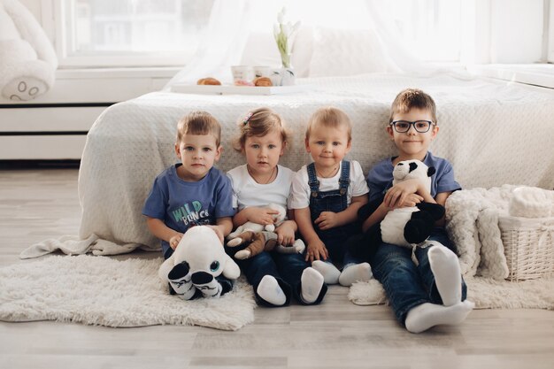 Picture of four little child in home clothes sits near the white sofa with toys, smile and have fun