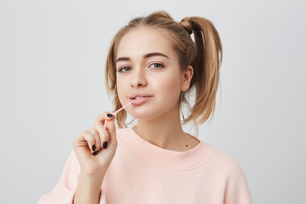 Picture of funny, playful, fashionable female student with appealing dark eyes, looking , enjoying free time at home after lectures at university. Cute girl stretching chewing gum.