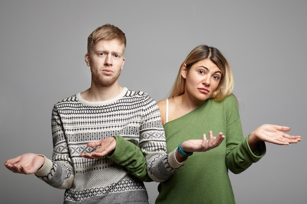 Picture of funny young couple man and woman having doubtful clueless looks, shrugging shoulders with open palms, feeling lost, looking in confusion and uncertainty. Body language