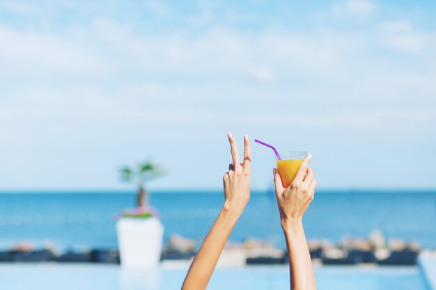 Picture of hands of girl holding cocktail on the sea background. It looks cool.