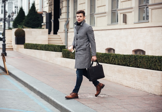 Free photo picture of handsome businessman with takeaway coffee in hand, crossing the street during sunny day