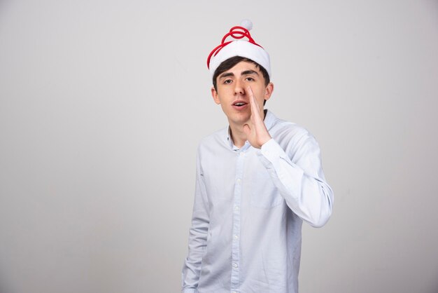 クリスマスの帽子に立って、口の近くで手をつないでいるハンサムな男の写真