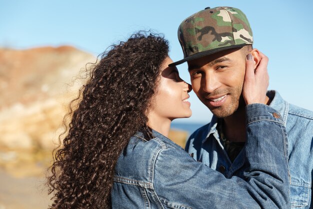 Picture of happy african loving couple walking outdoors at beach. Woman kissing a boy cheek.