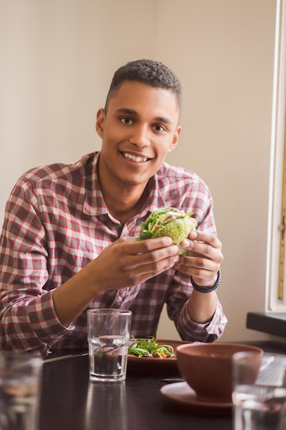 Picture of happy man eating vegan burger in vegan restaurant or cafe Smiling man sitting at table and looking at camera