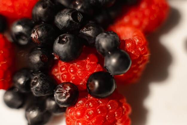 Picture of juicy fresh ripe red raspbberries and blueberries in a white ceramic plate with light background