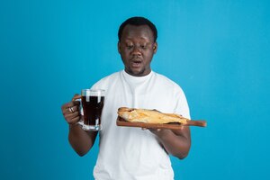 Free photo picture of a man in white t-shirt holding dried fish with a glass mug of wine against blue wall