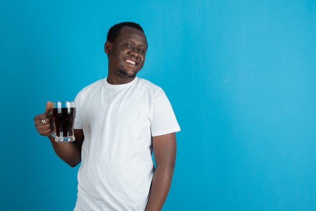 Picture of a man in white t-shirt holding a glass mug of wine against blue wall