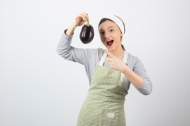 Picture of a nice young woman model in apron pointing at an eggplant