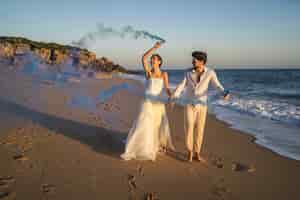 Бесплатное фото Фотография красивой пары, позирующей с голубой дымовой шашкой на пляже
