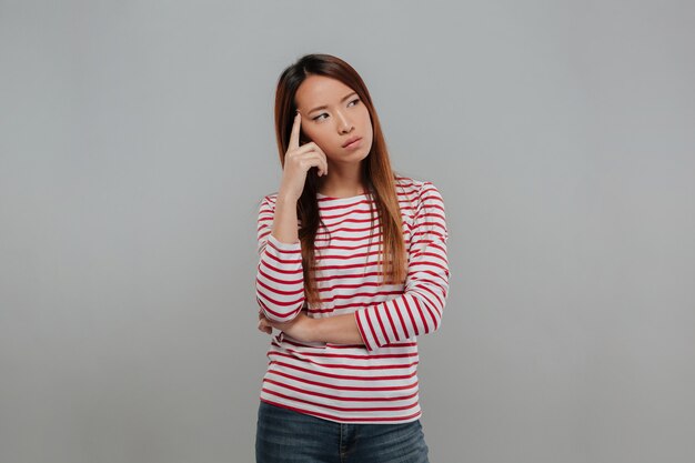Picture of pensive asian woman in sweater looking away over gray background