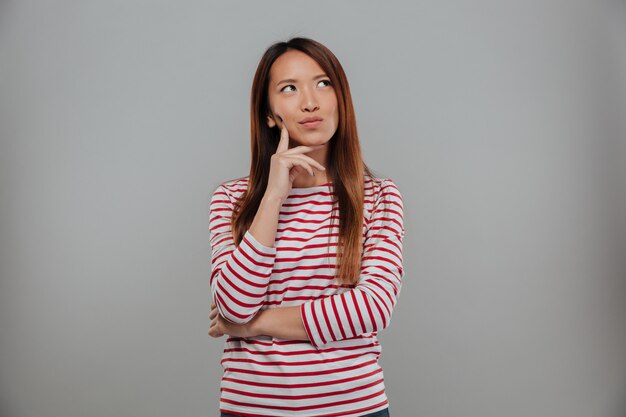 Picture of Pensive asian woman in sweater looking up over gray background