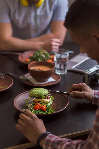 Picture of people sitting in vegan cafe or restaurant and eating tasty vegetarian sandwich