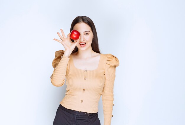 Picture of a pretty woman model standing and holding fresh red apple .