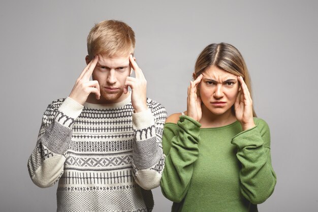 Picture of serious concentrated young man and woman in casual clothes frowning and squeezing temples as if trying to remember something or having terrible headache. Human facial expressions