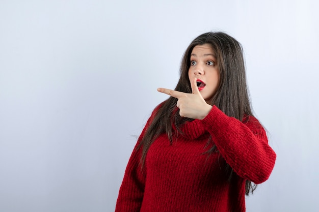 Immagine di una giovane donna scioccata con un maglione rosso che punta lontano