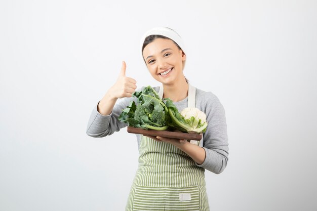 Picture of a smiling attractive woman with a wooden plate of cauliflowers showing a thumb up 