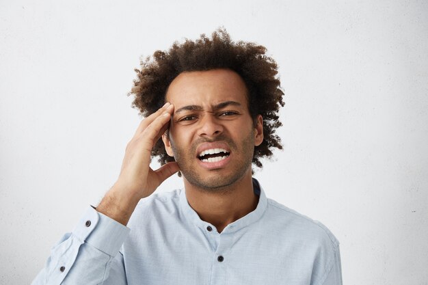 Picture of stressed young employee in formal shirt having headache