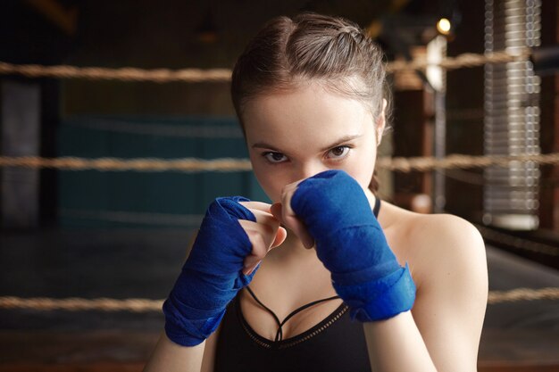 Picture of stylish 18 year old woman boxer with strong arms and athletic fit body working out indoors, mastering punching skills and techniques