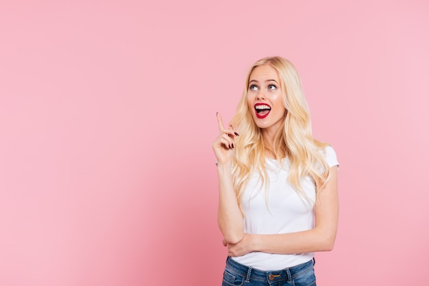 Picture of Surprised blonde woman having idea and looking up over pink 