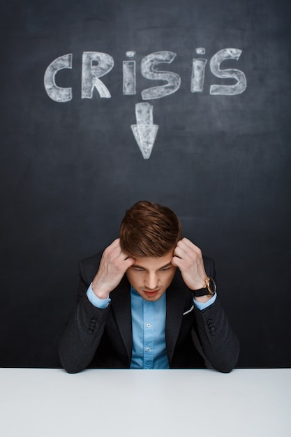 Picture of tired man over blackboard with crisis inscription