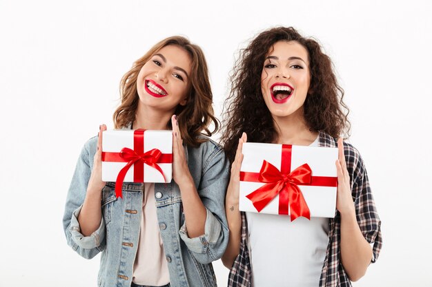 白い壁の上の手で贈り物を保持している2つの幸せな女の子の写真