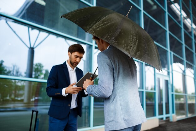 雨の駅で話している2人の若いビジネスマンの写真