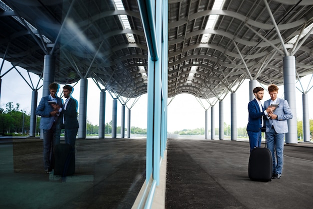 Foto gratuita un'immagine di due giovani uomini d'affari che parlano sulla stazione e che tengono la compressa ha riflesso in finestra