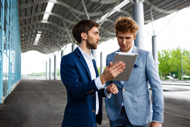 Picture of  two young businessmen talking on station  and holding tablet