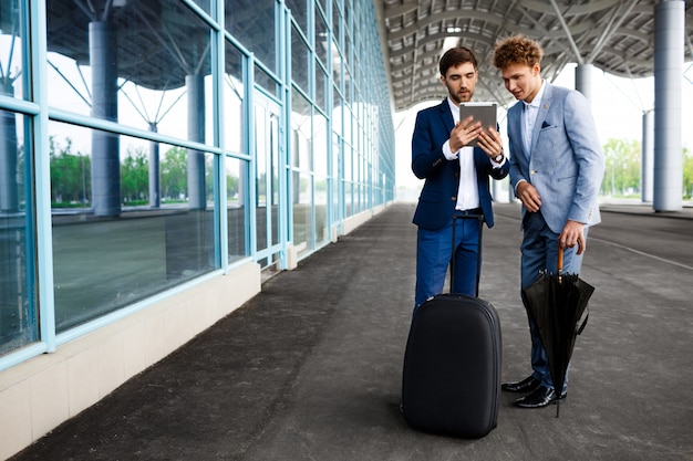 Free photo picture of  two young businessmen talking on station  and holding tablet