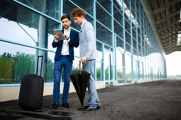 Изображение двух молодых бизнесменов, говорить на терминале и держа планшет