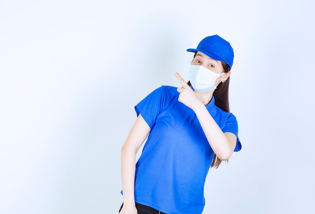 Picture of woman in uniform and medical mask pointing up. 