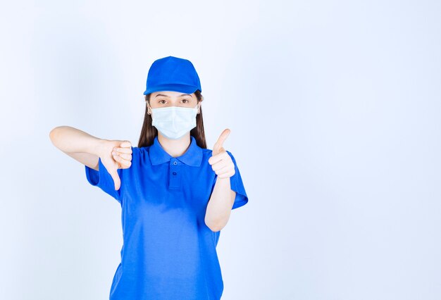 Picture of woman in uniform and medical mask showing thumb down . 