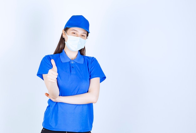 親指を上に見せている制服と医療マスクの女性の写真。