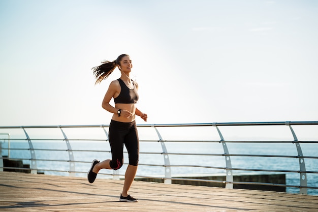 Picture of young attractive fitness woman running with sea on wall