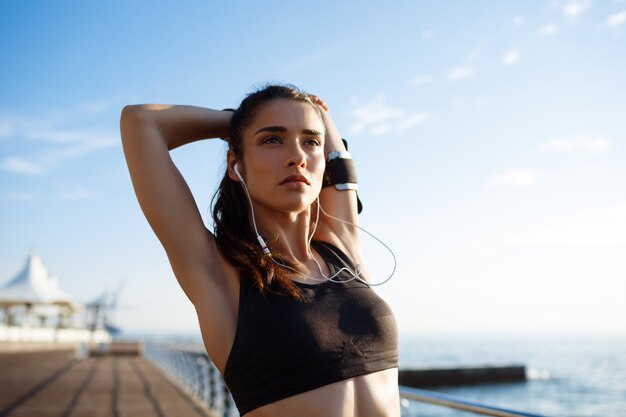 Picture of young beautiful fitness woman makes sport exercises with sea coast on wall