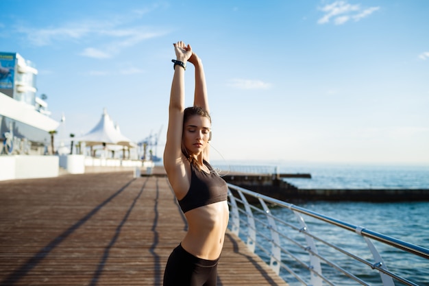 Picture of young beautiful fitness woman makes sport exercises with sea coast on wall