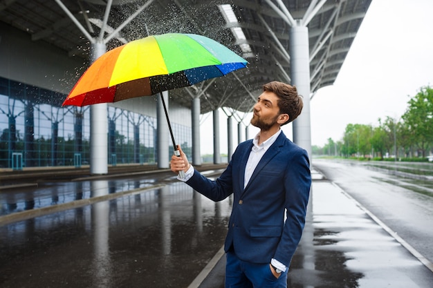 비오는 거리에서 주위에 뿌리와 화려한 우산을 들고 젊은 사업가의 그림