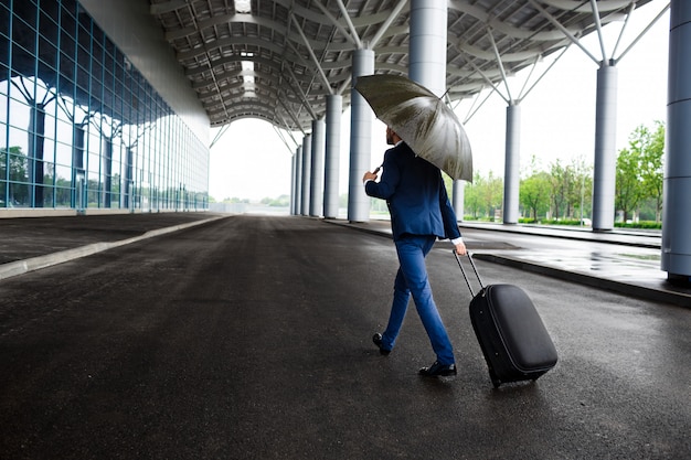 Picture of  young  businessman holding  suitcase and umbrella at rainy terminal