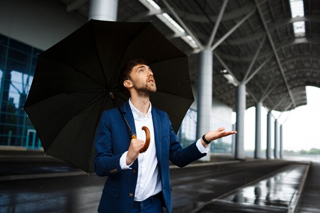 Picture of  young  businessman holding  umbrella in rain looking up at drops