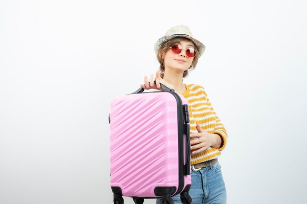 분홍색 여행 가방을 들고 모자를 쓴 젊은 여성 관광객의 사진. 고품질 사진