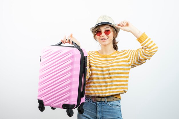 Picture of a young female tourist in hat holding pink travel suitcase . High quality photo
